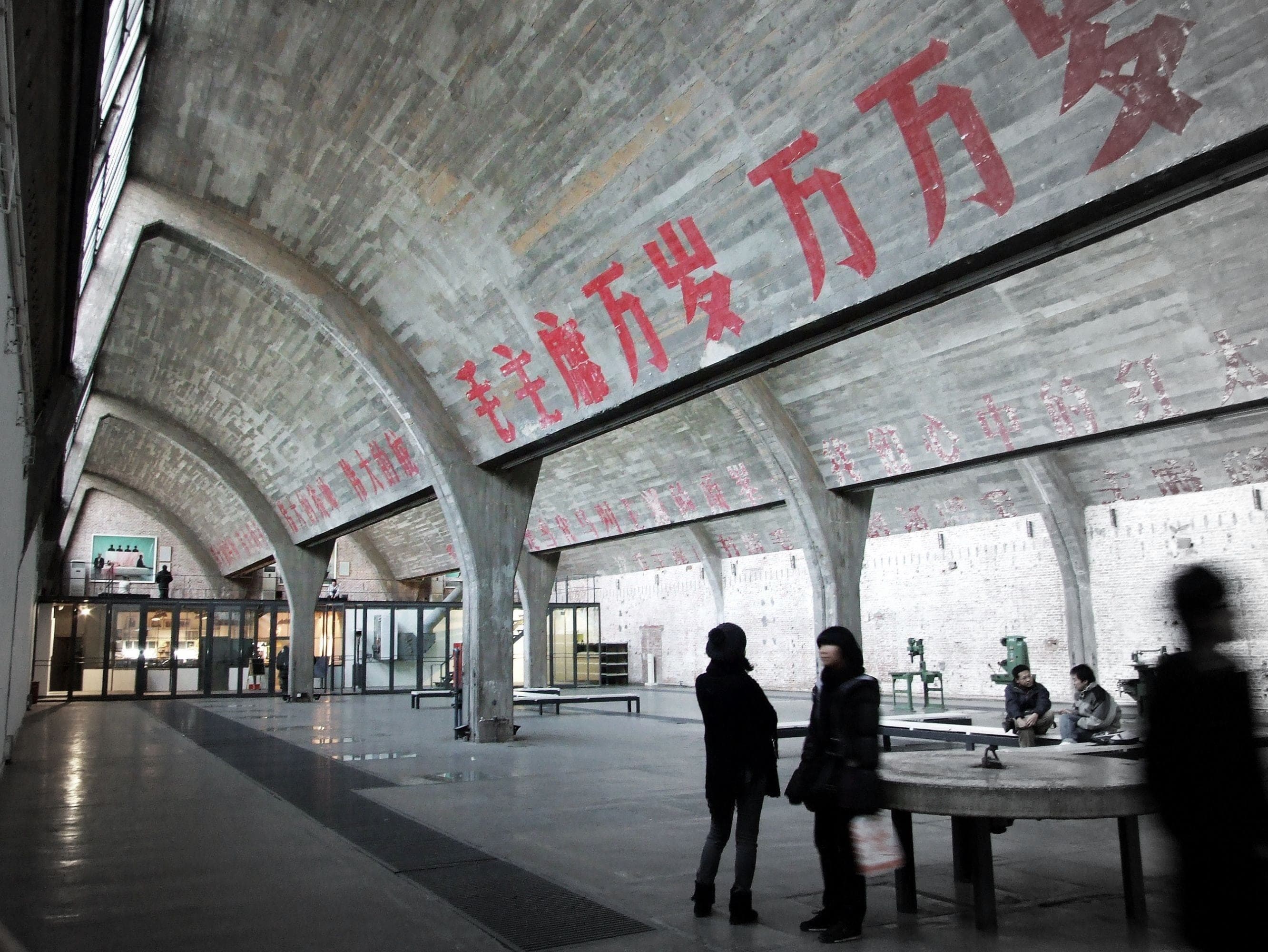 A converted Bauhaus factory hall in Beijing's 798 Art District, a contemporary art installation visible through the open shutter doors