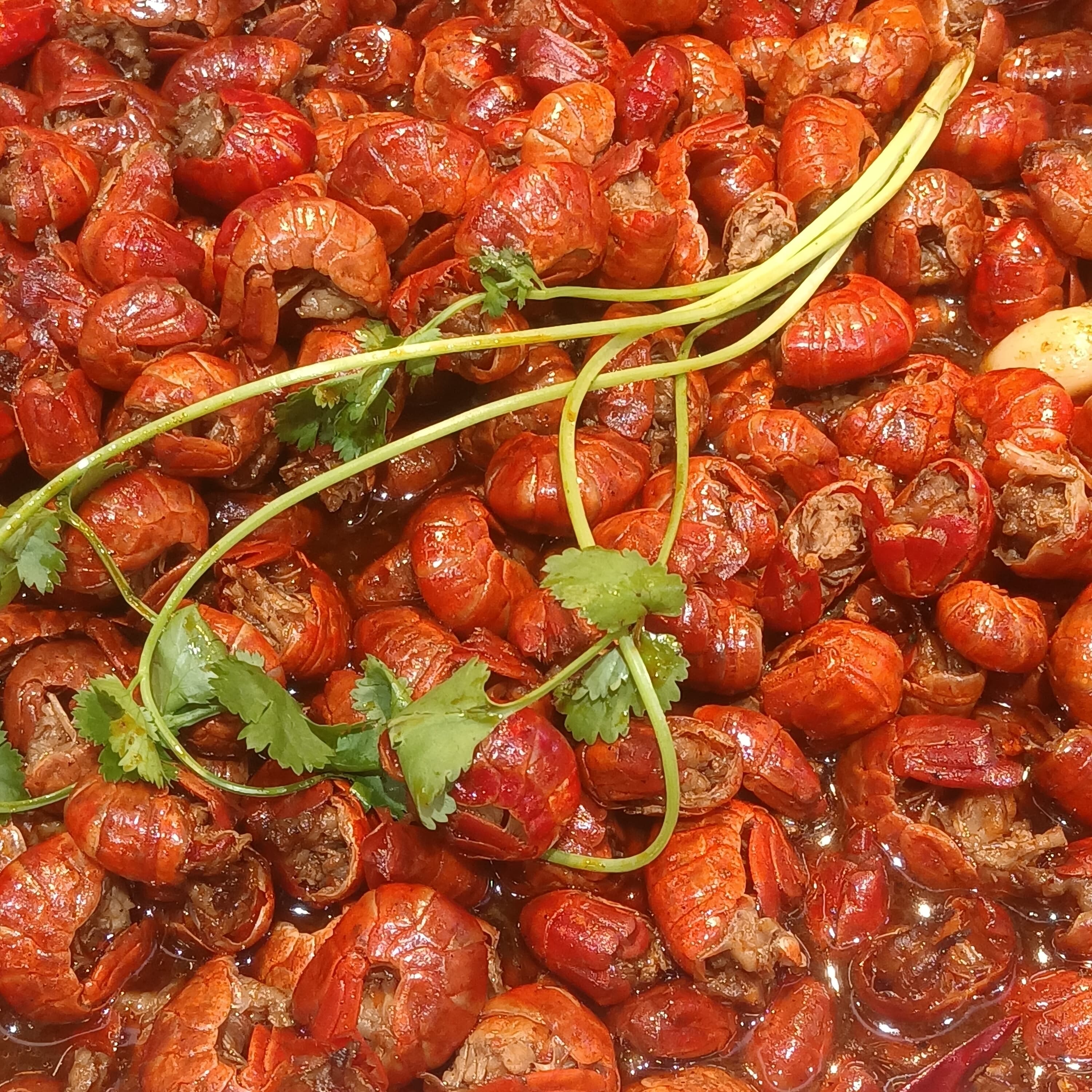 A pile of Changsha kouwei xia crayfish in glossy red chilli sauce with garlic, perilla leaves and beer foam still on the rim, served on a metal platter