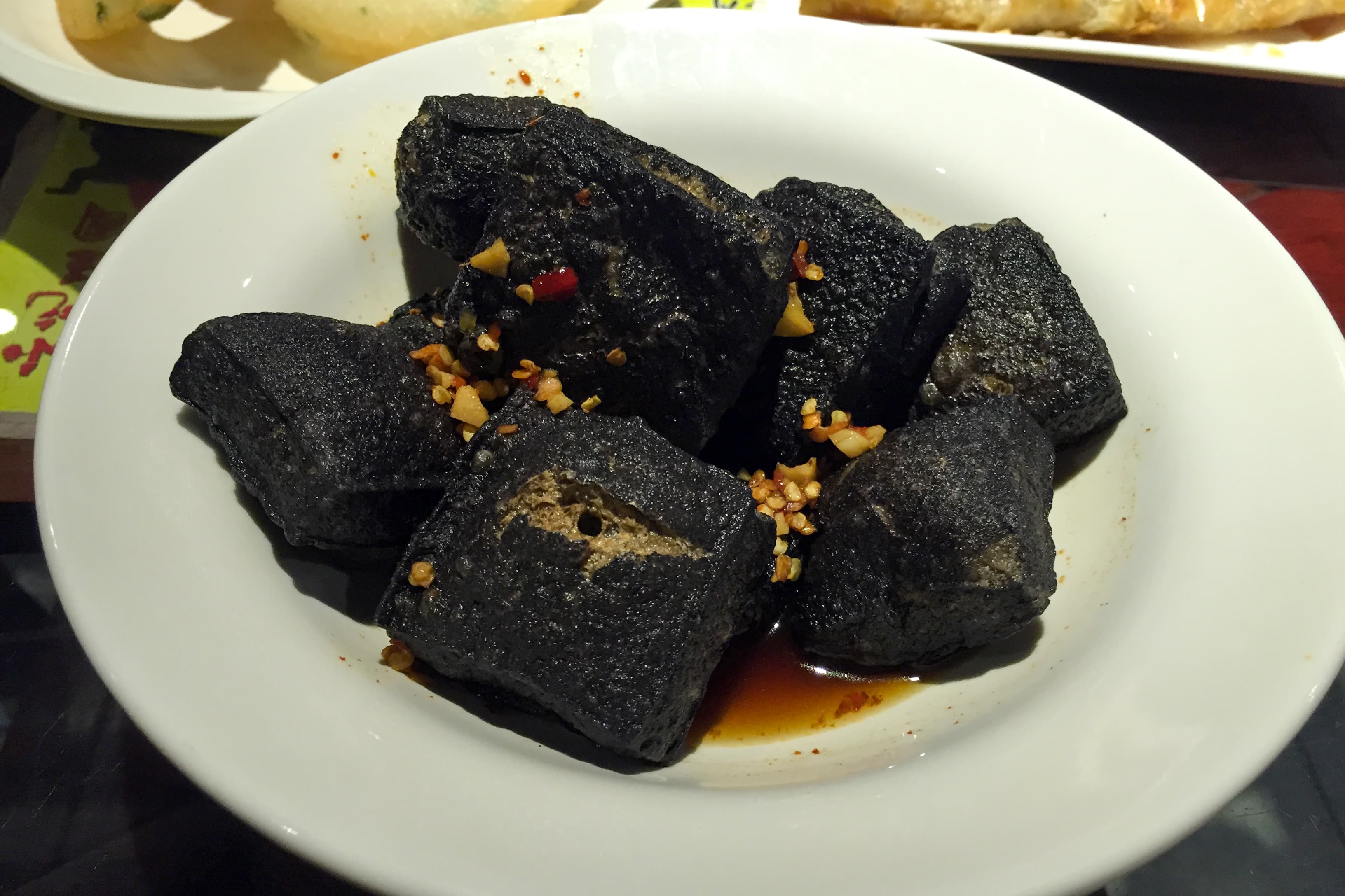 Mahogany-black Changsha-style stinky tofu cubes glossed with red chilli oil, garlic-leek sauce and cilantro at a Wuyi Square food stall