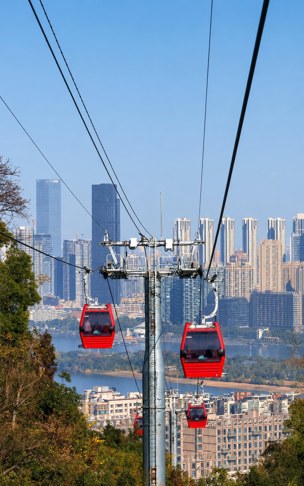 重建后的岳麓山索道红色玻璃缆车穿越山脊，脚下湘江流过，对岸长沙天际线远展