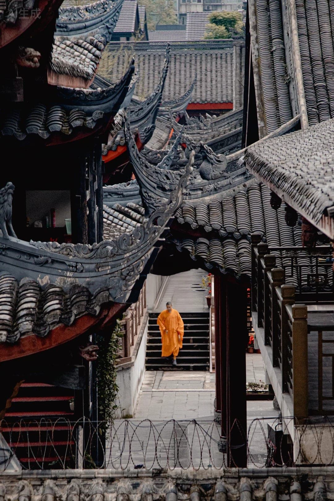 A monk in orange robes on the steps of Daci Temple, tiled rooflines folding around the courtyard