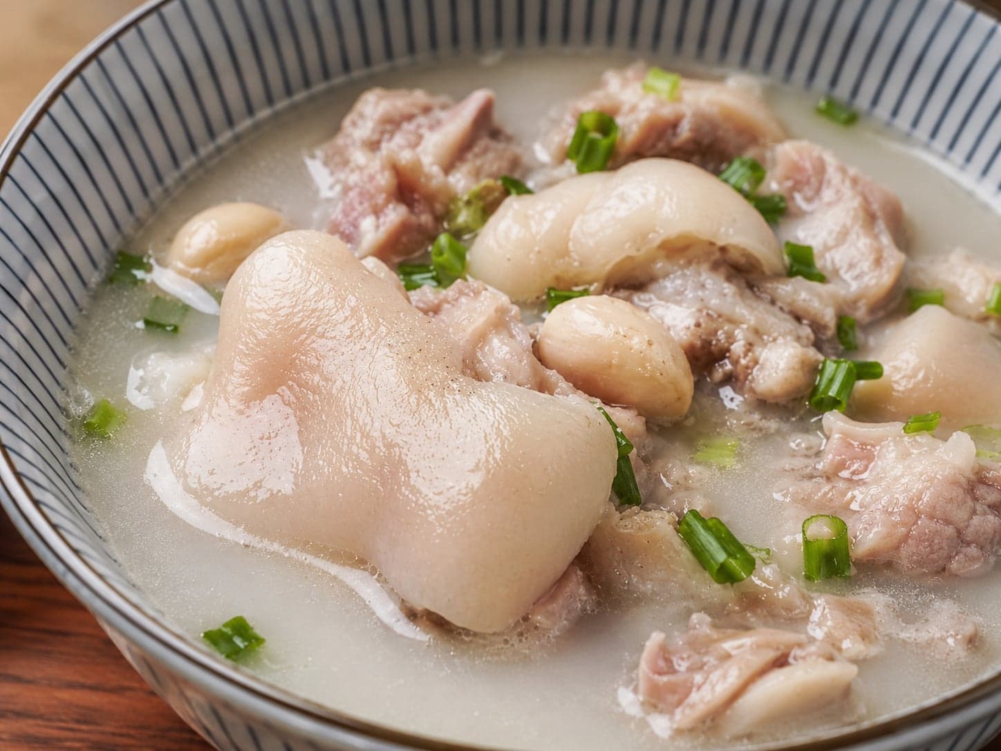A wide bowl of milky-white pig trotter soup with white kidney beans, beside a small dish of chilli-and-Sichuan-pepper dip on a Chengdu late-night table