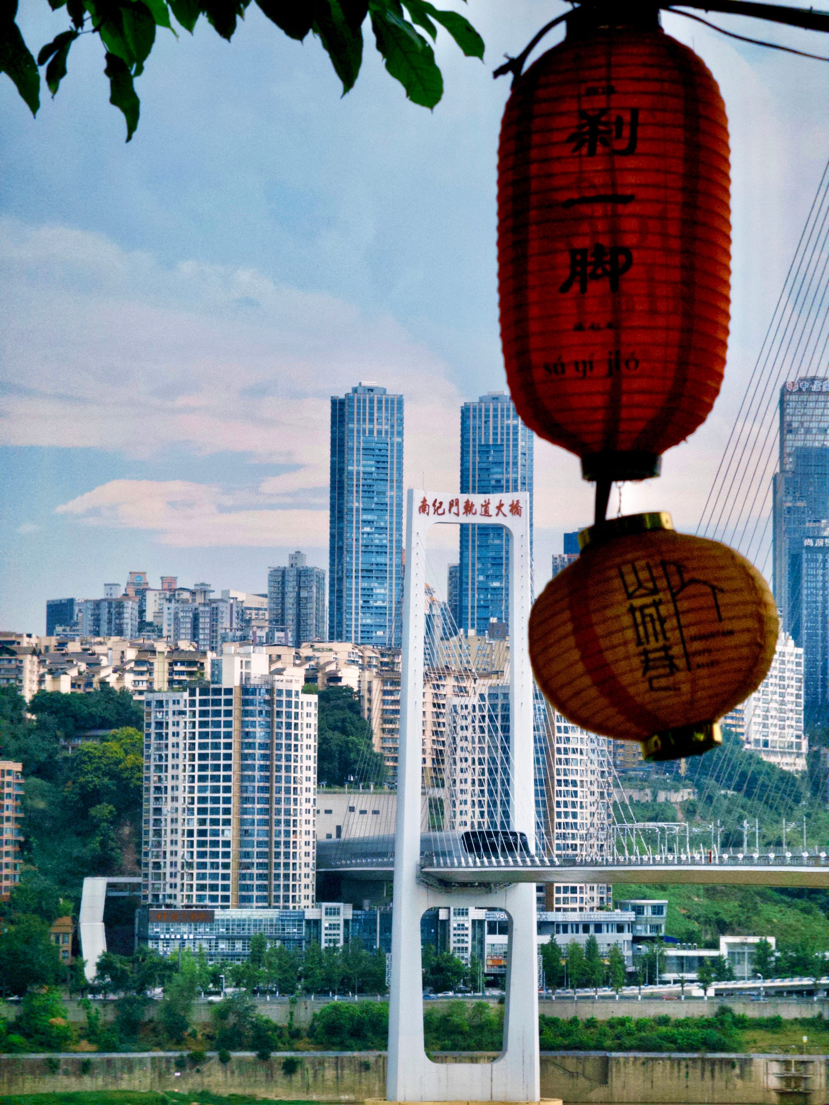 An aerial view of the Mountain City Footpath in Chongqing, the spiral elevated walkway curving down through forest above the Yangtze with city blocks beyond