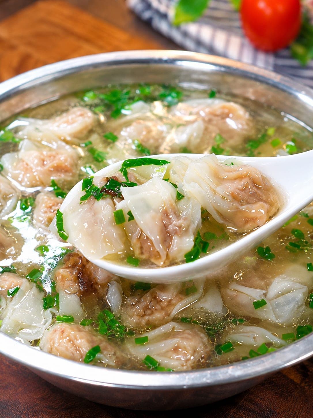 A bowl of Fuzhou rou yan in clear broth scattered with chives, the pork-paste-wrapped wonton lifted on a spoon