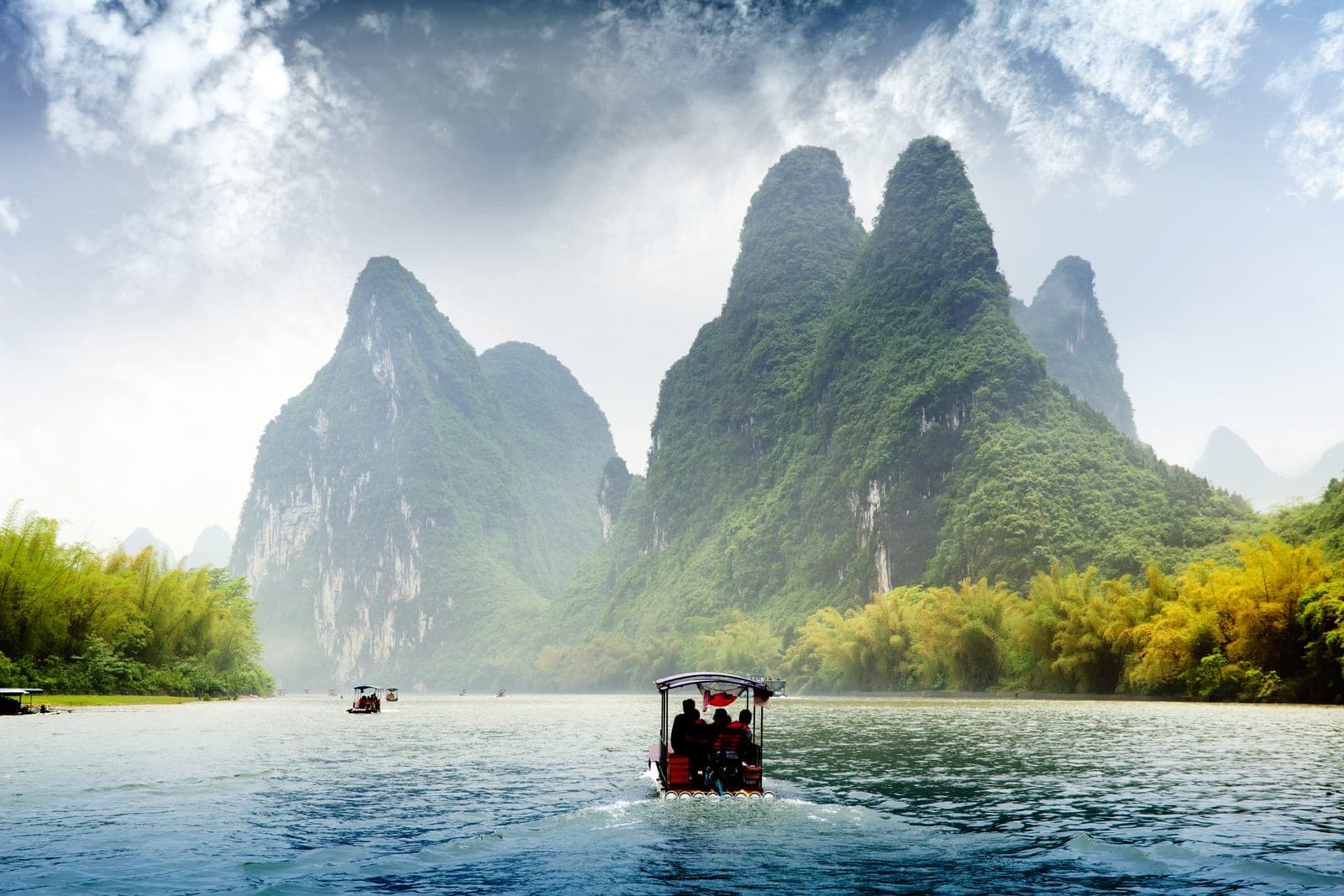 A small private river vessel drifting under misty karst peaks on the Li River