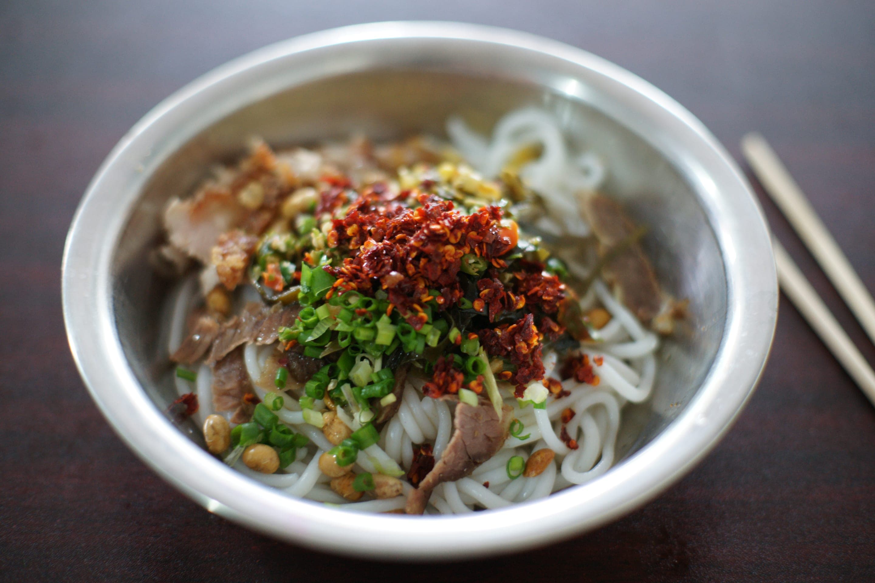 A bowl of Guilin rice noodles topped with sliced beef, scallion, chilli oil and peanuts