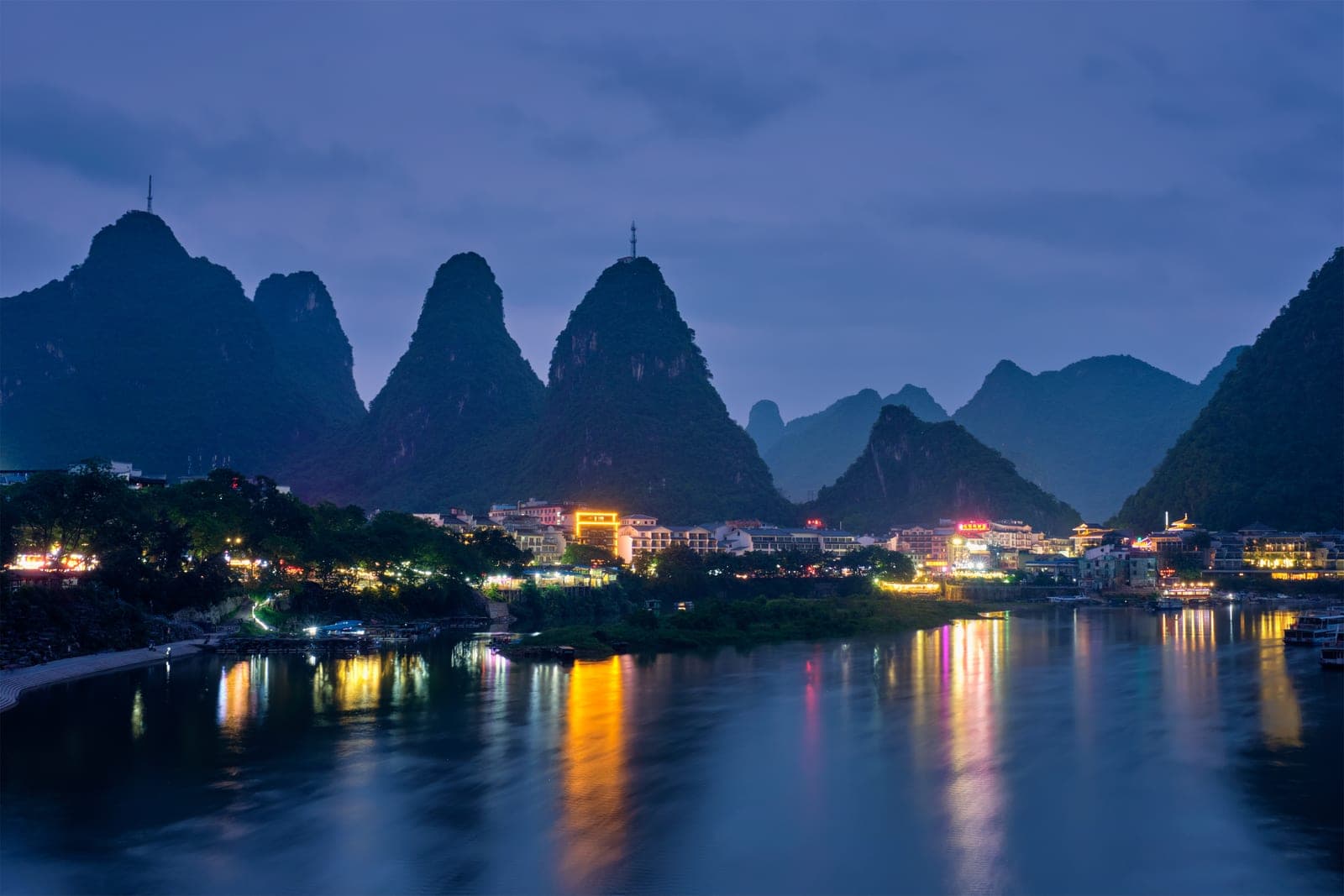 Yangshuo town centre illuminated at dusk, the lights of West Street reflecting on the Li River with karst peaks silhouetted behind