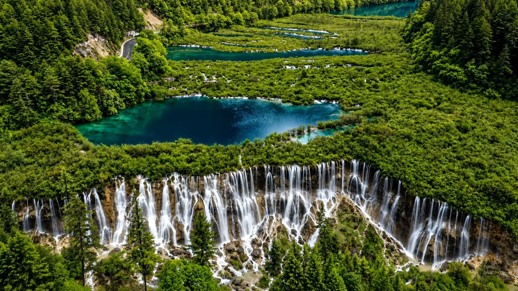 自高处俯瞰九寨沟诺日朗瀑布，一道宽阔的钙华水帘沿长长台阶层层而下，上方湖泊与两侧密林清晰可见