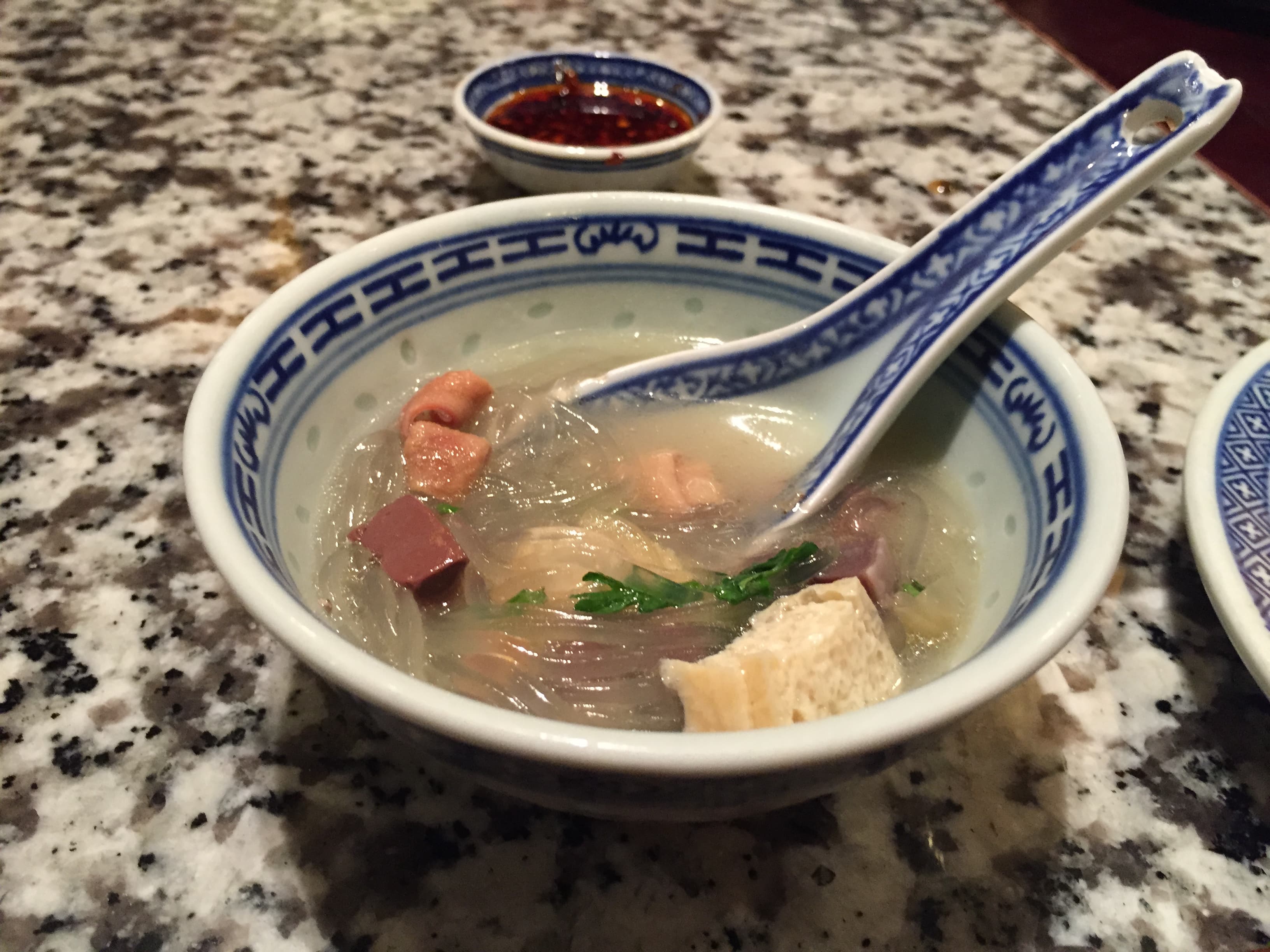 青花白瓷碗中的南京鸭血粉丝汤：滑嫩鸭血块、红薯粉丝与葱花