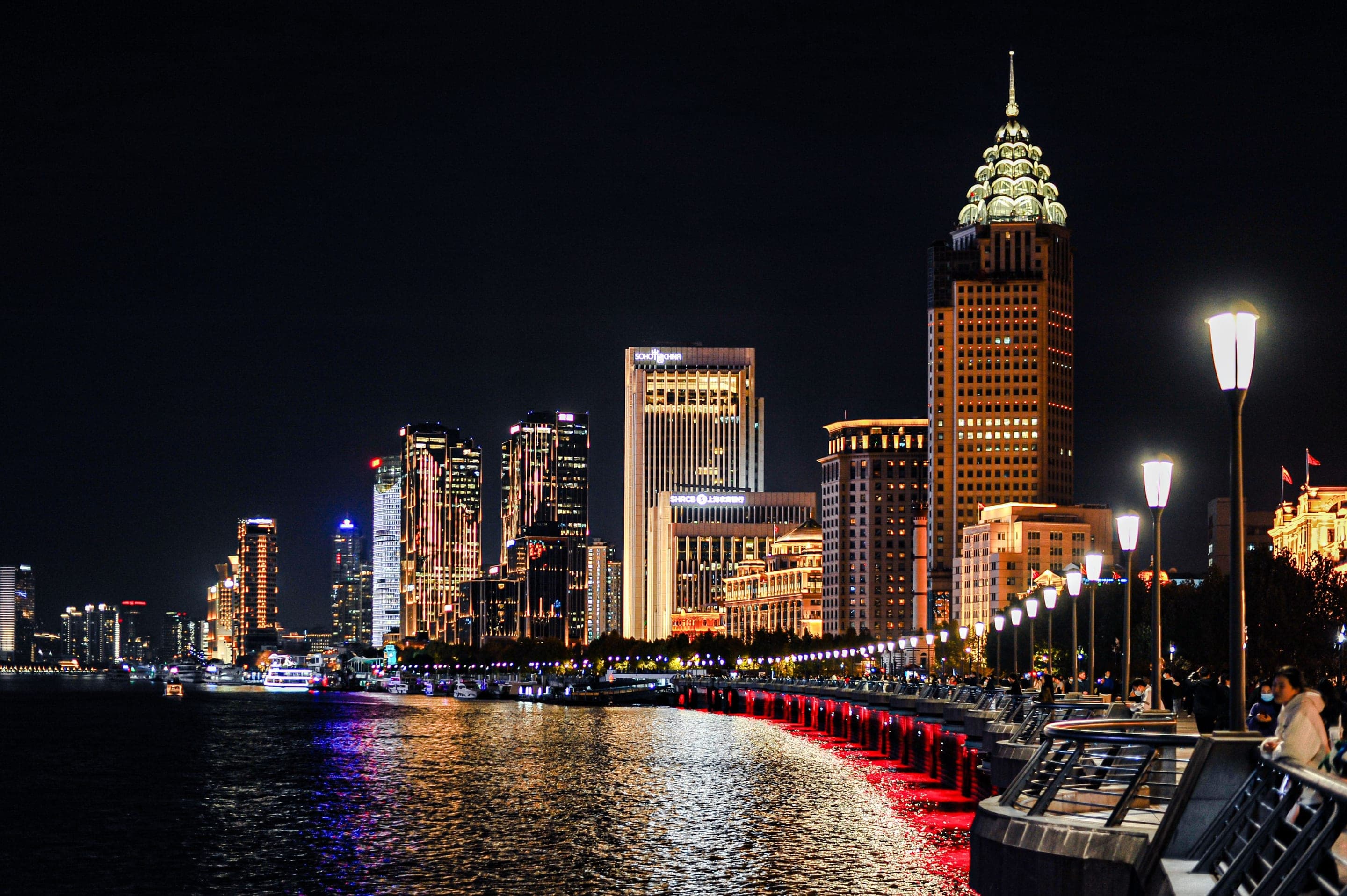 The Pudong skyline viewed across the Huangpu from the Bund promenade at night, the Oriental Pearl Tower, Shanghai Tower and Shanghai World Financial Center lit and reflected in the river