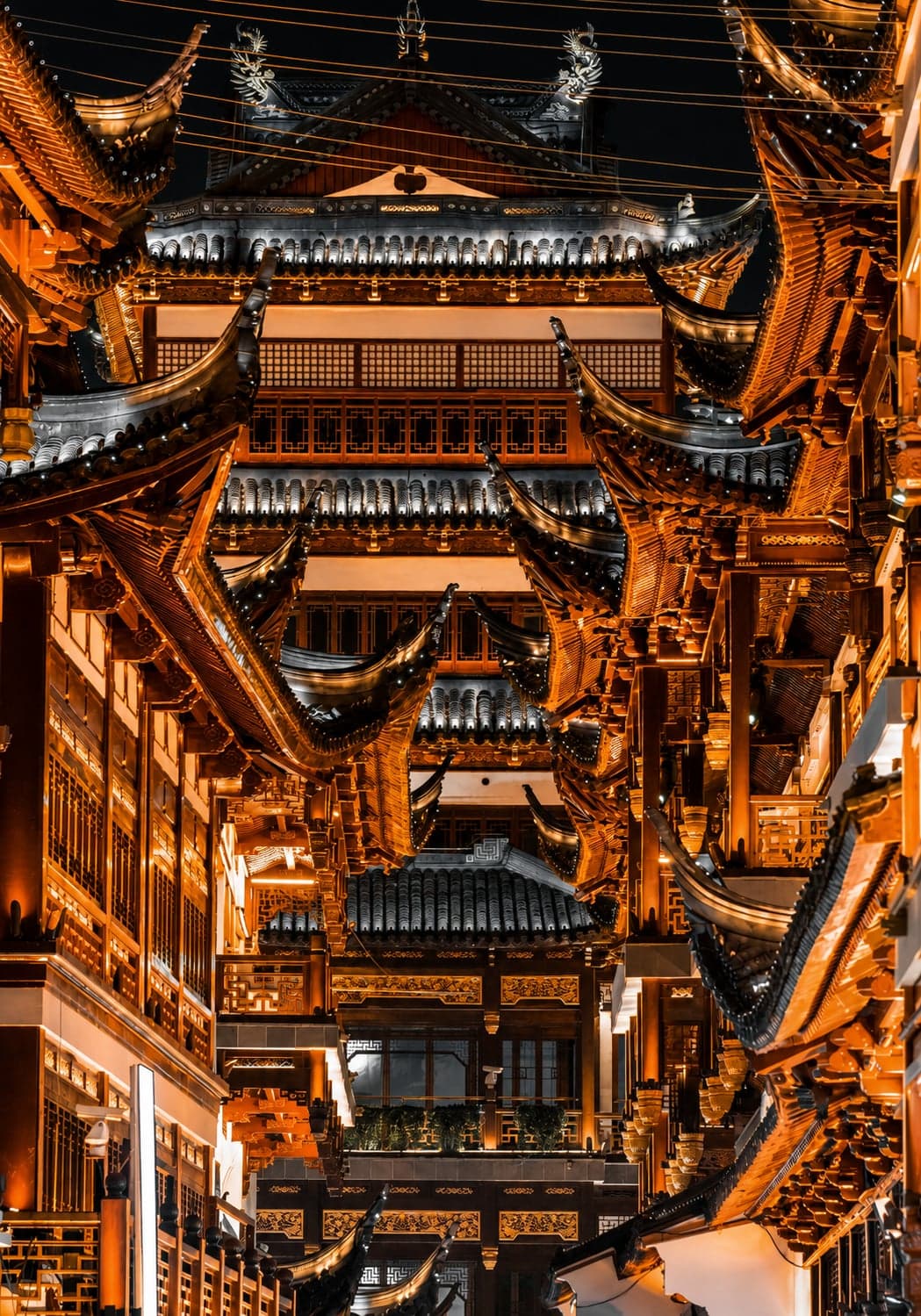 Layered Ming-style upturned eaves at night in Shanghai's Nanshi old town, warmly lit and stacked tier over tier around the City God Temple