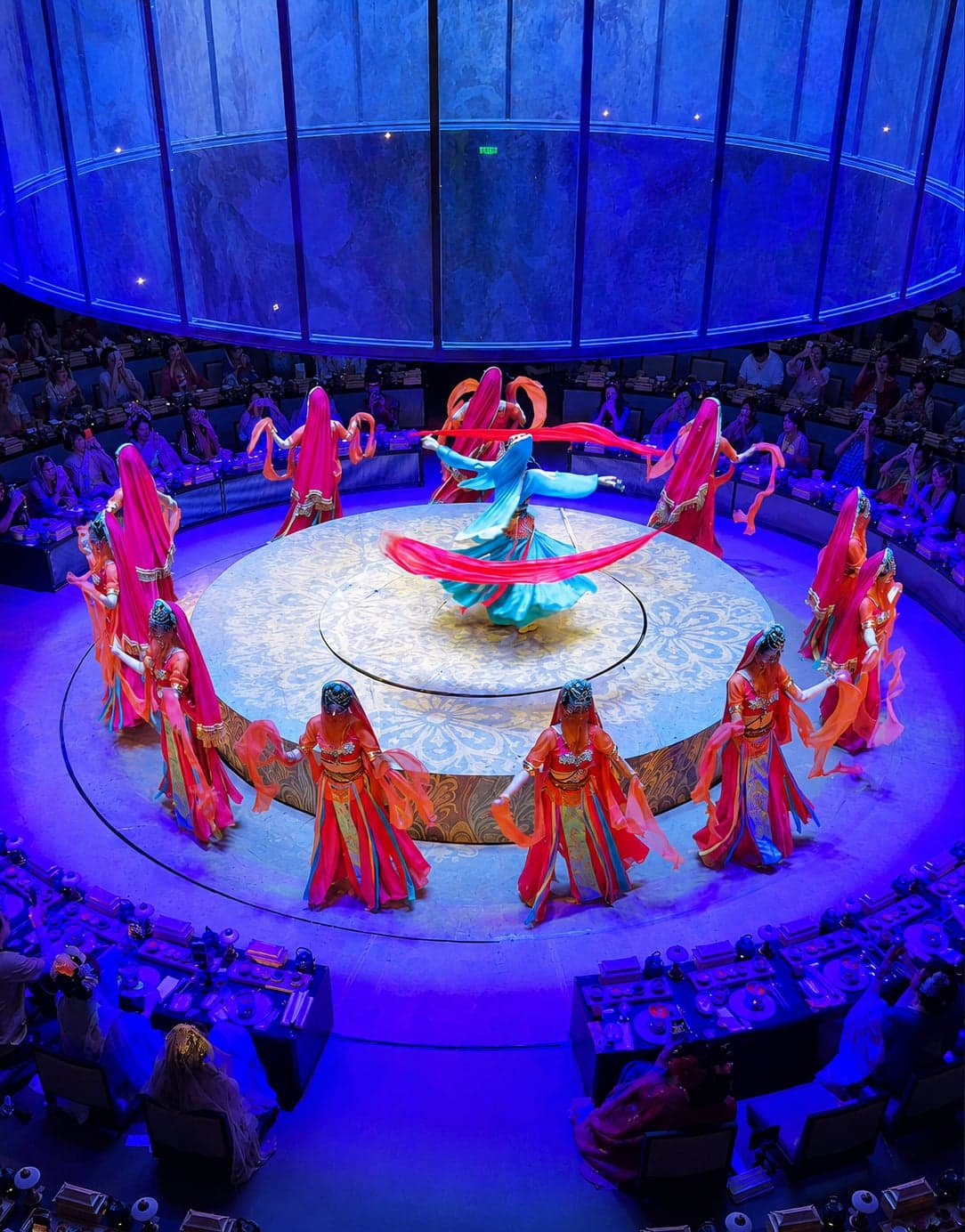 A circular stage at SILK GALA in Suzhou, a solo dancer with a red silk ribbon at centre and a ring of performers around the perimeter, with the audience seated for dinner on the outer tiers