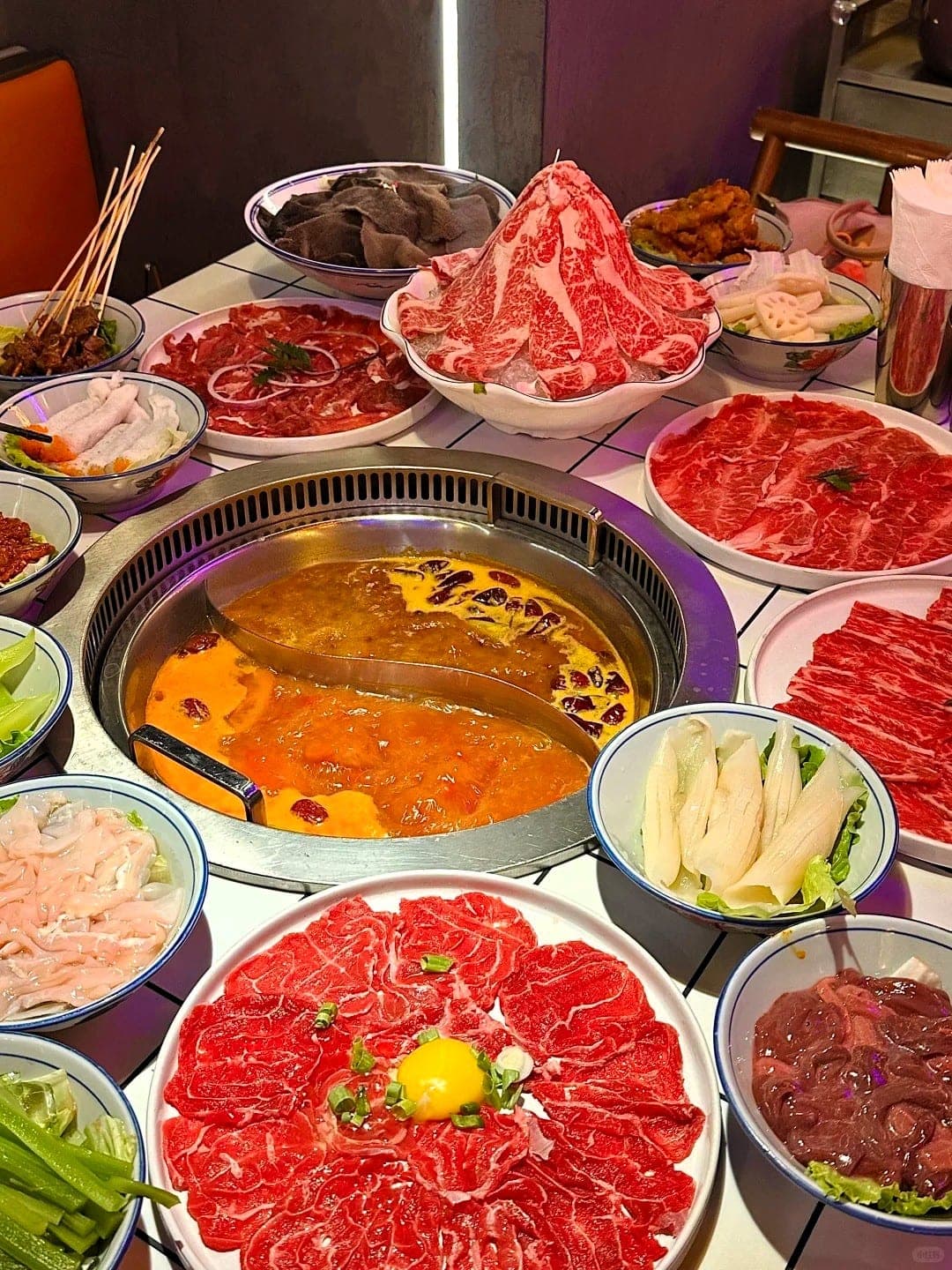 A Chengdu hot pot table, split broth bubbling at the centre surrounded by plates of thin-sliced beef, skewers and fresh greens