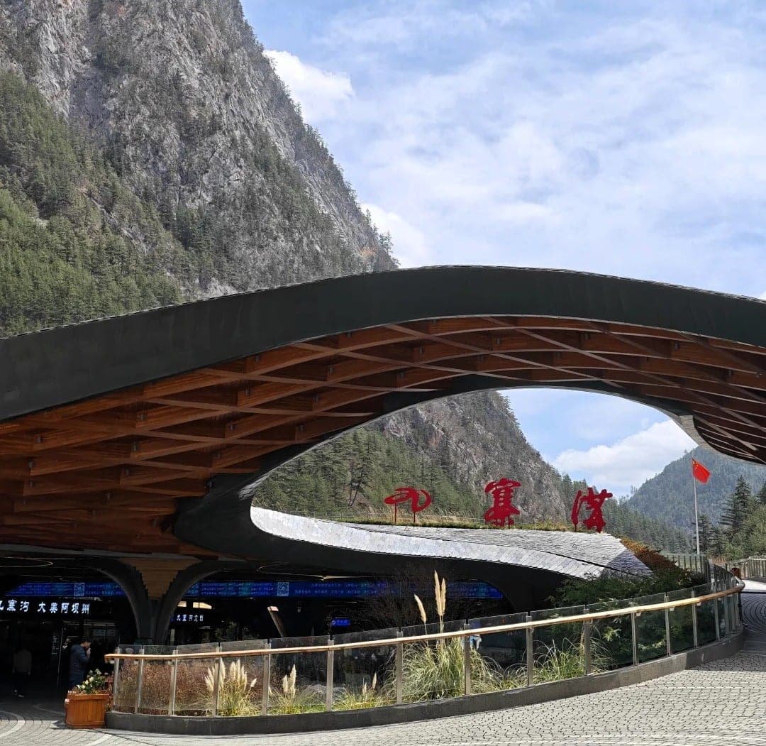 The curved timber canopy of the Jiuzhaigou park gate, latticed beams sweeping above the ticket hall with forested cliffs rising behind