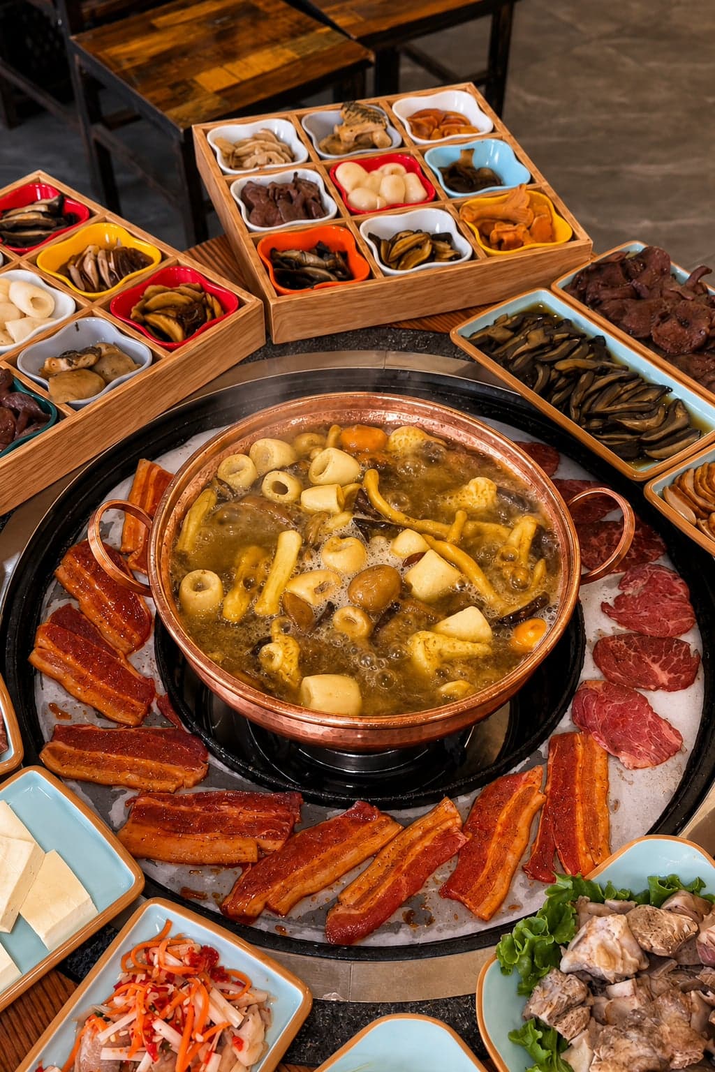 Yunnan wild mushroom hotpot, a brass pot of clear chicken-bone broth beside a tray of sliced mushroom varieties in compartments