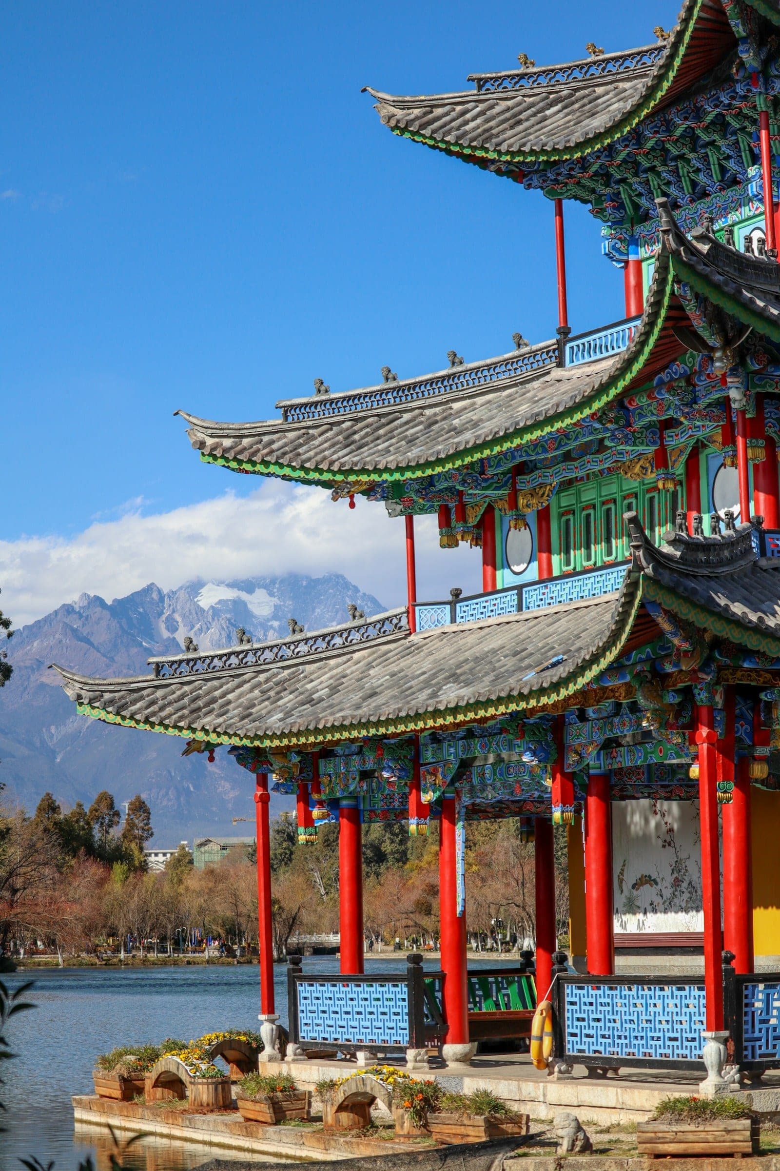 A stone bridge over a willow-shaded canal in Lijiang Old Town, with tiled rooftops behind