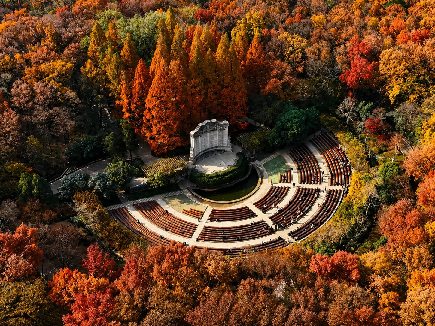 自空中俯瞰中山陵音乐台,半圆扇形石阶与弧形照壁尽收一画,秋色山林环抱其侧