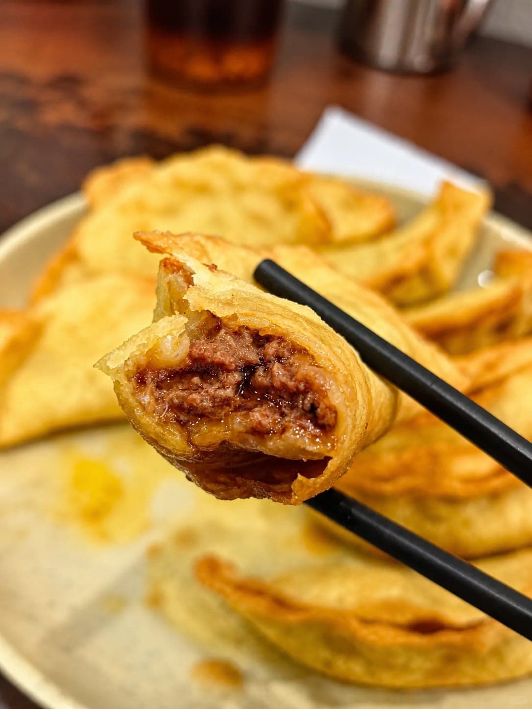 一只刚咬开的牛肉锅贴举于筷间,金黄漆面碎口可见,里头手剁牛肉与肉汁尽显,盘中其余仍在身后