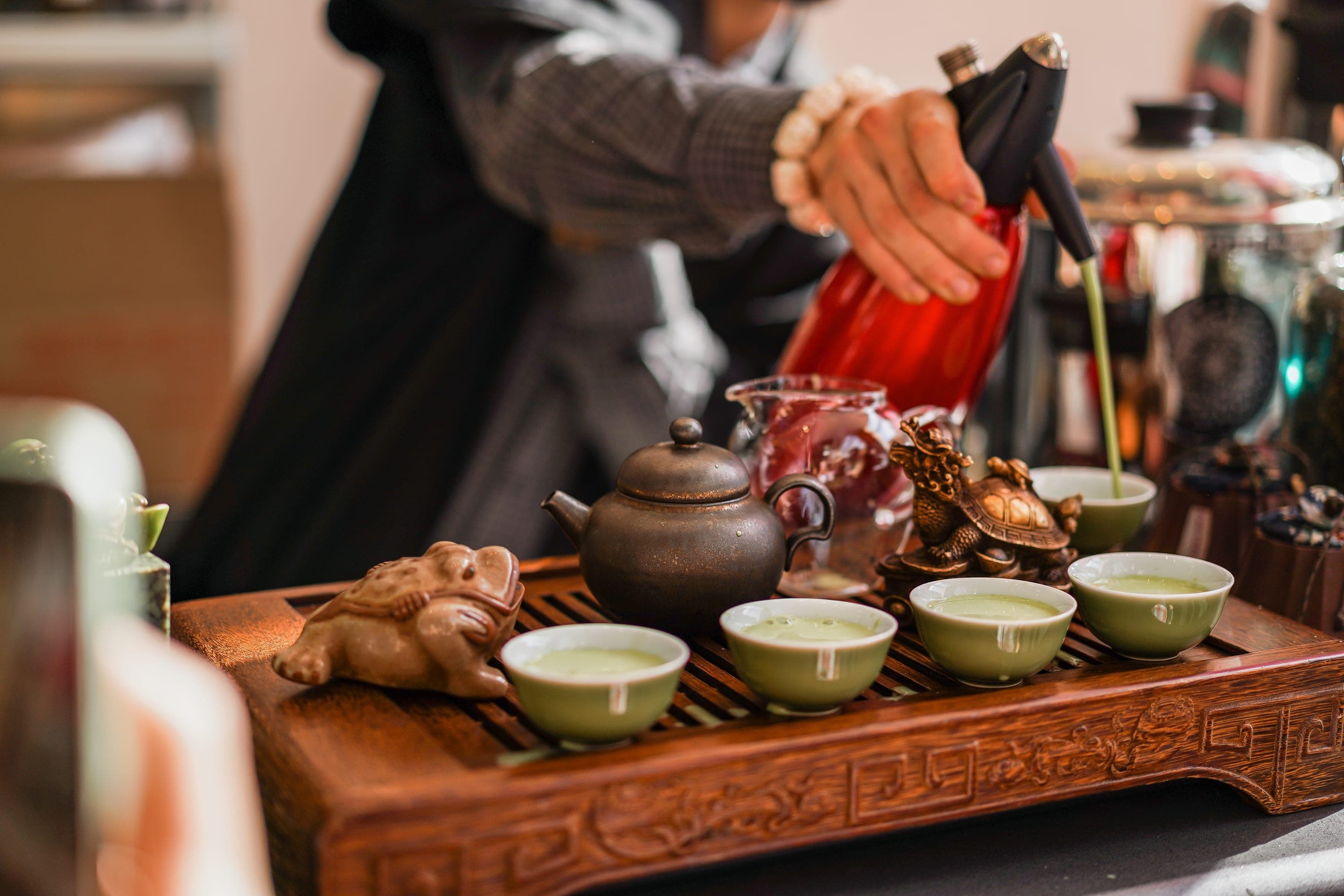Green tea poured from a long-spout kettle into small cups on a wooden tray at a Chengdu tea house