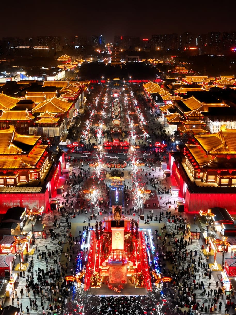 Datang Everbright City after dusk: reproduction Tang pavilions and bronze statuary lit along the pedestrian axis beside the Big Wild Goose Pagoda, Xi'an