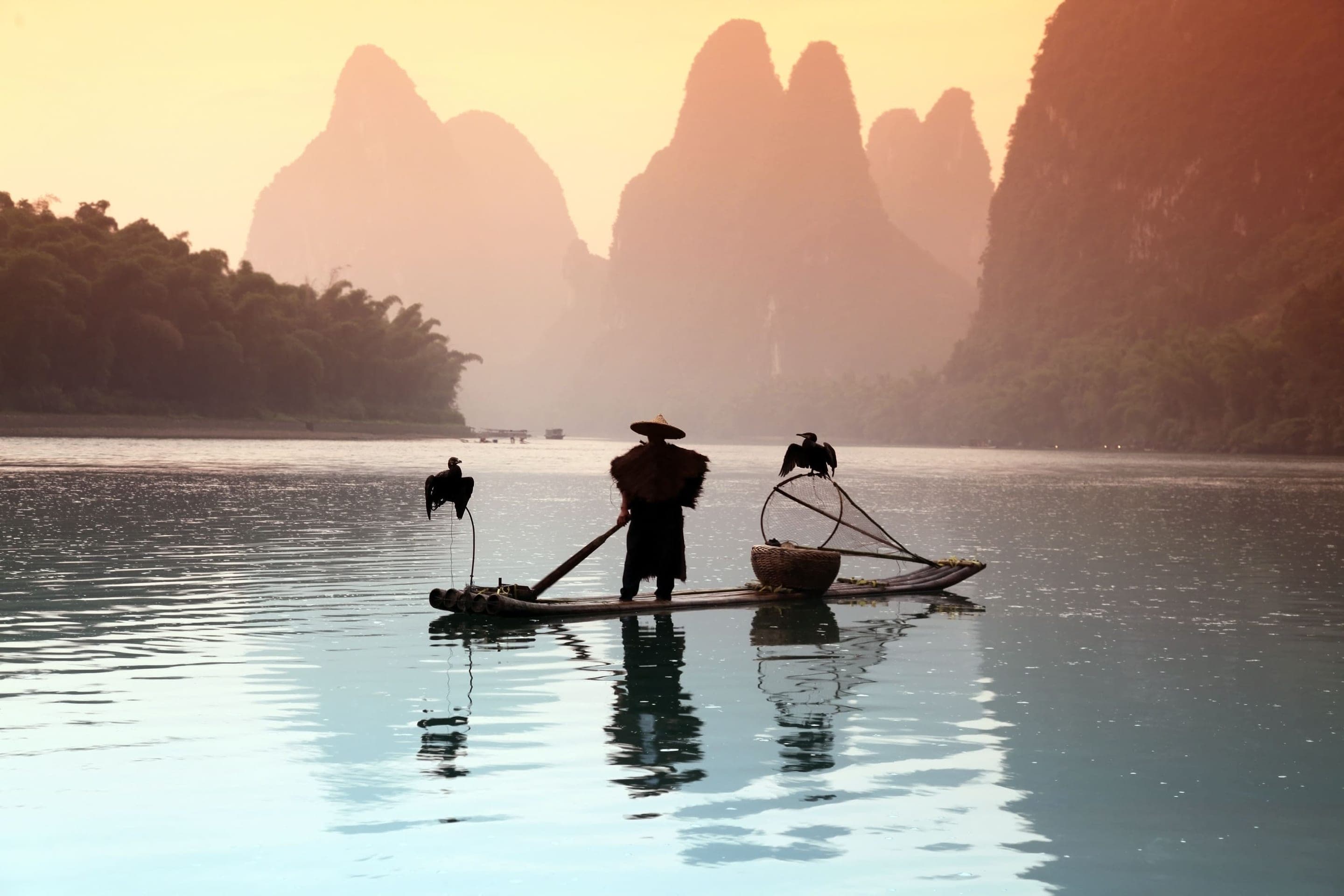 Cormorant fisherman with kerosene lamp on a bamboo raft at dusk