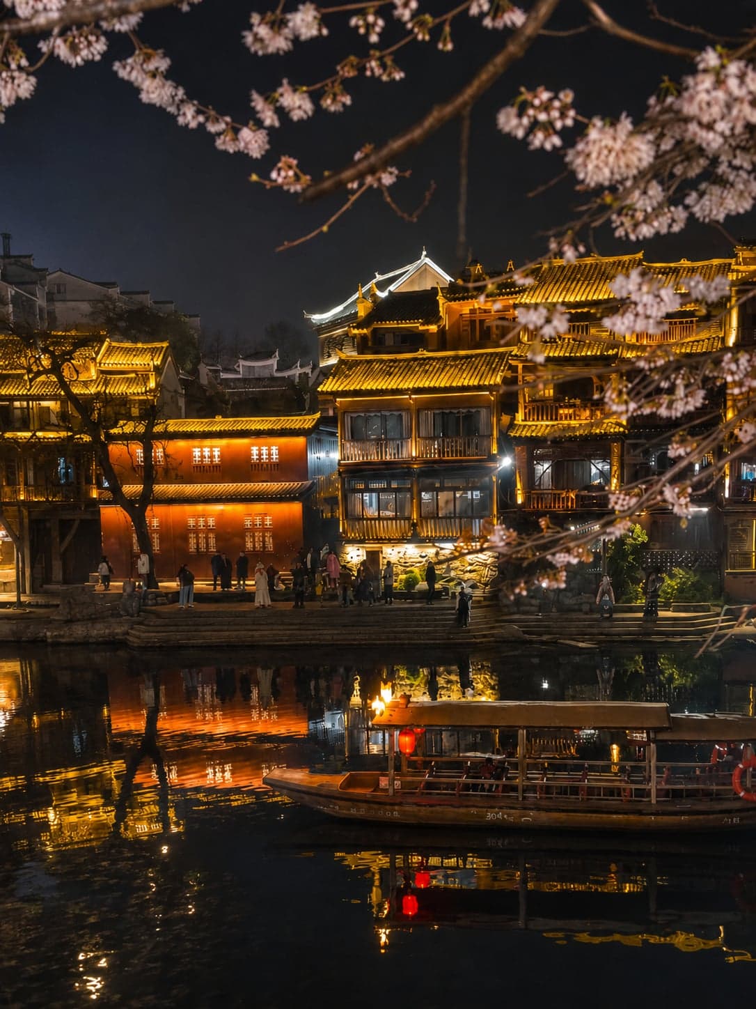 A wooden flat-bottom boat poling upstream on the Tuojiang at dusk, lanterns lit along the stilt houses on both banks of Fenghuang Ancient Town