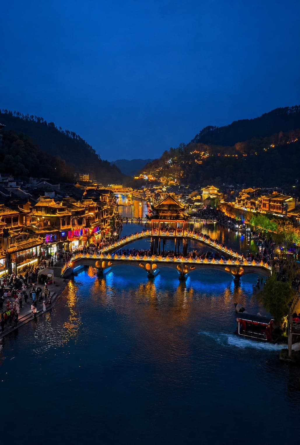 Stilted Diaojiaolou houses leaning out over the Tuojiang River at Fenghuang Ancient Town, with lanterns lit along both banks at dusk