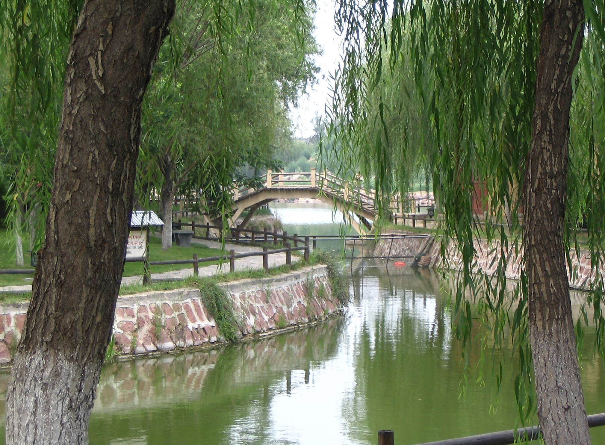 A wooden Rainbow Bridge and costumed Song-era performers in the open-air Qingming Riverside Park, Kaifeng