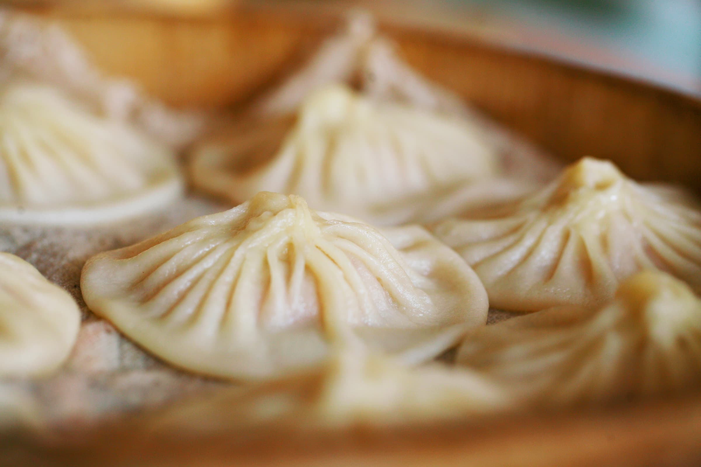 A bamboo steamer of Kaifeng Guan Tang Bao soup dumplings with paper-thin pleated dough, a small dish of dark vinegar and shredded ginger on the side