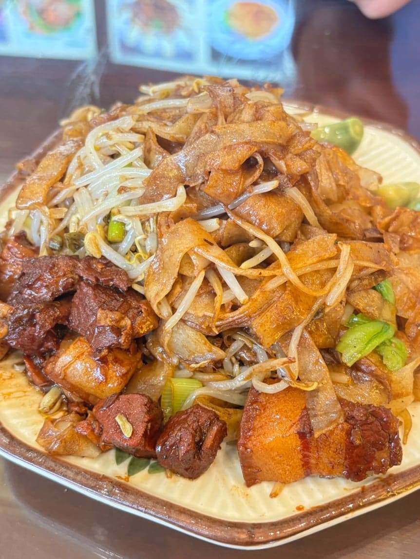 一盘冒着热气的郑州焖饼:金黄宽条饼丝、白净豆芽与油亮的坛子肉块同堆于盘中