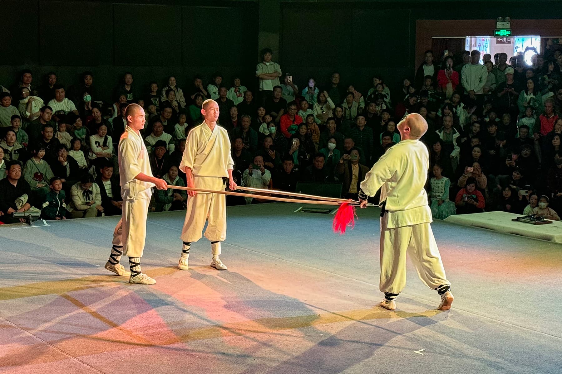 A Shaolin monk-trained performer mid-air over a spinning staff on the timber floor of the on-site training hall at Shaolin Temple, Dengfeng