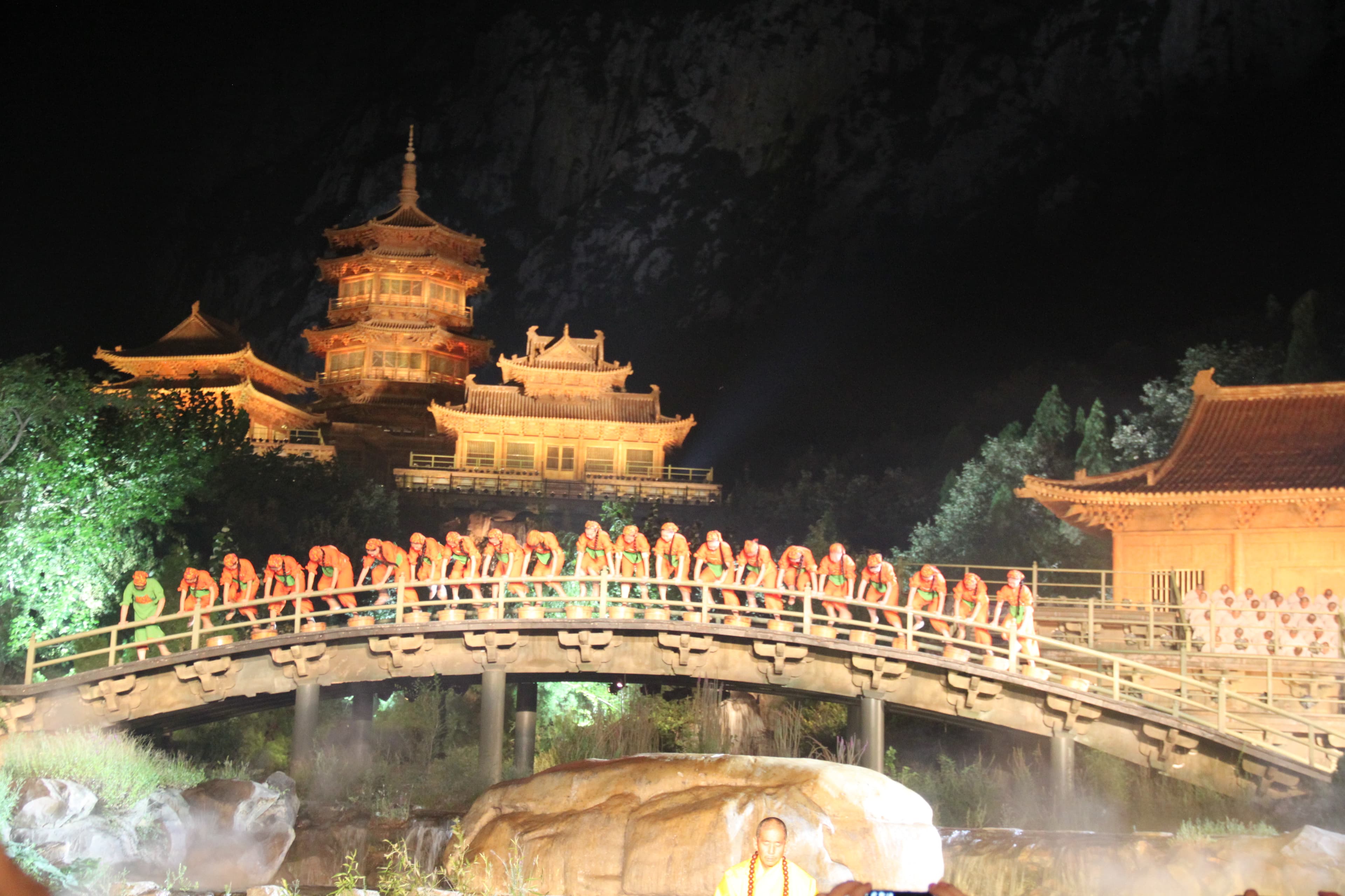 Performers spread across the Daixiangou gorge stage near Shaolin Temple with cliff face lit in gold behind, the open-air Zen Music Shaolin ceremony, Dengfeng