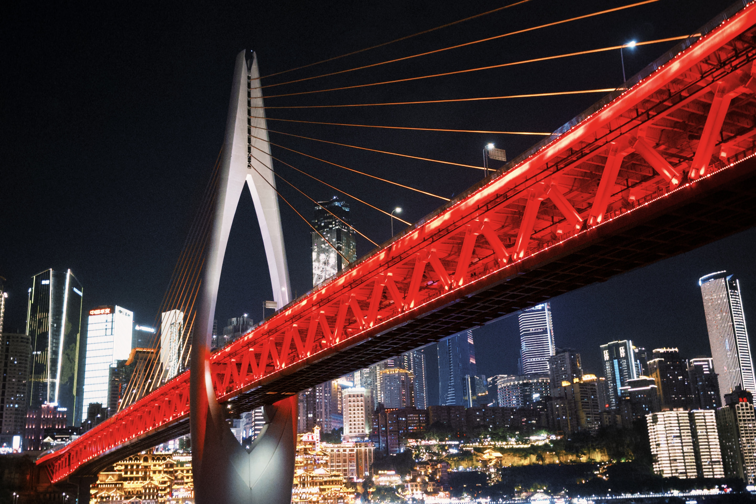 Dongshuimen Bridge lit red at night, with Chongqing's skyline and Hongya Cave behind